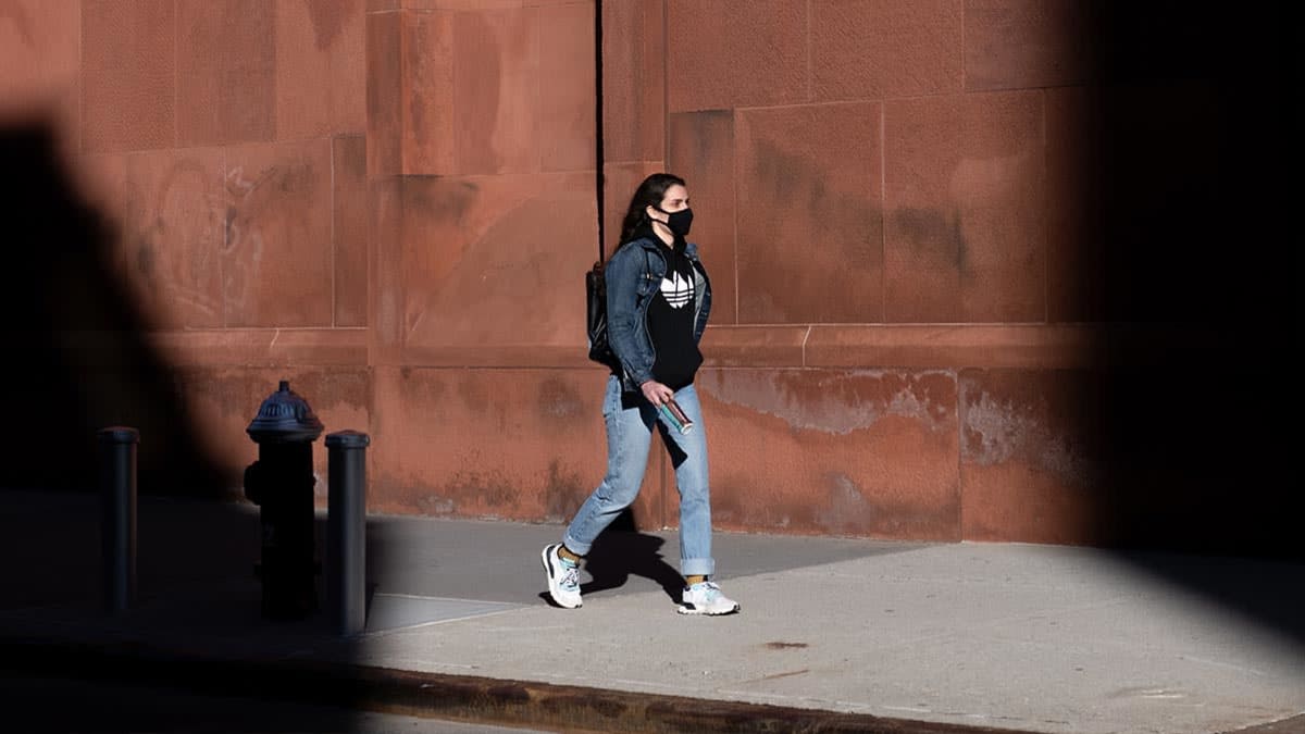 woman wearing a mask walks through a patch of sunlight on March 29, 2021 in New York City. After undergoing various shutdown orders for the past 12 months the city is currently in phase 4 of its reopening plan, allowing for the reopening of low-risk outdoor activities, movie and television productions, indoor dining as well as the opening of movie theaters, all with capacity restrictions. (Photo by Alexi Rosenfeld/Getty Images)