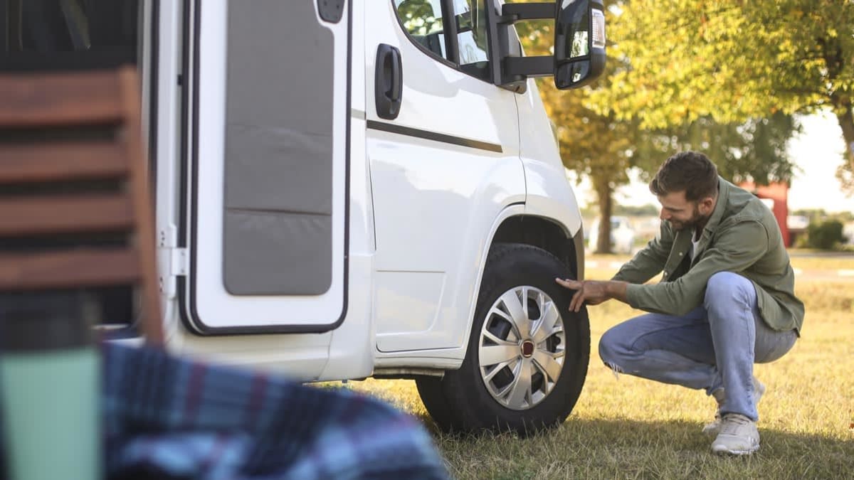 A person kneeling down inspecting an RV tire