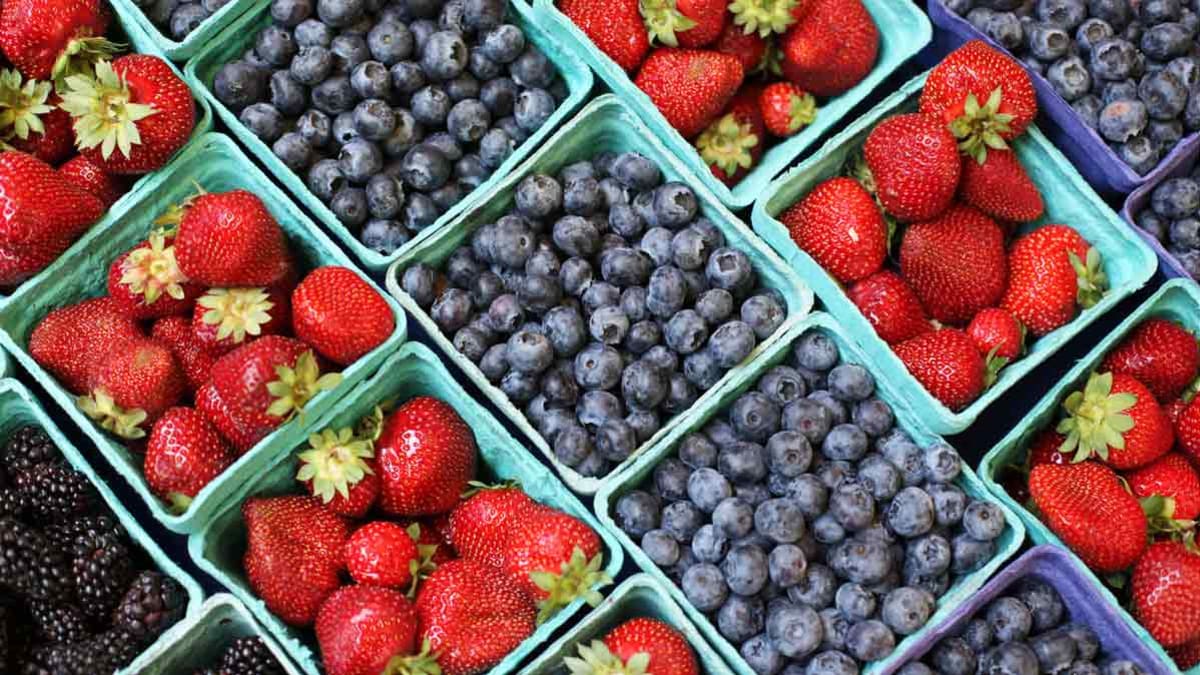 From left to right, blackberries, strawberries, blueberries, strawberries, and blueberries sit in light blue baskets