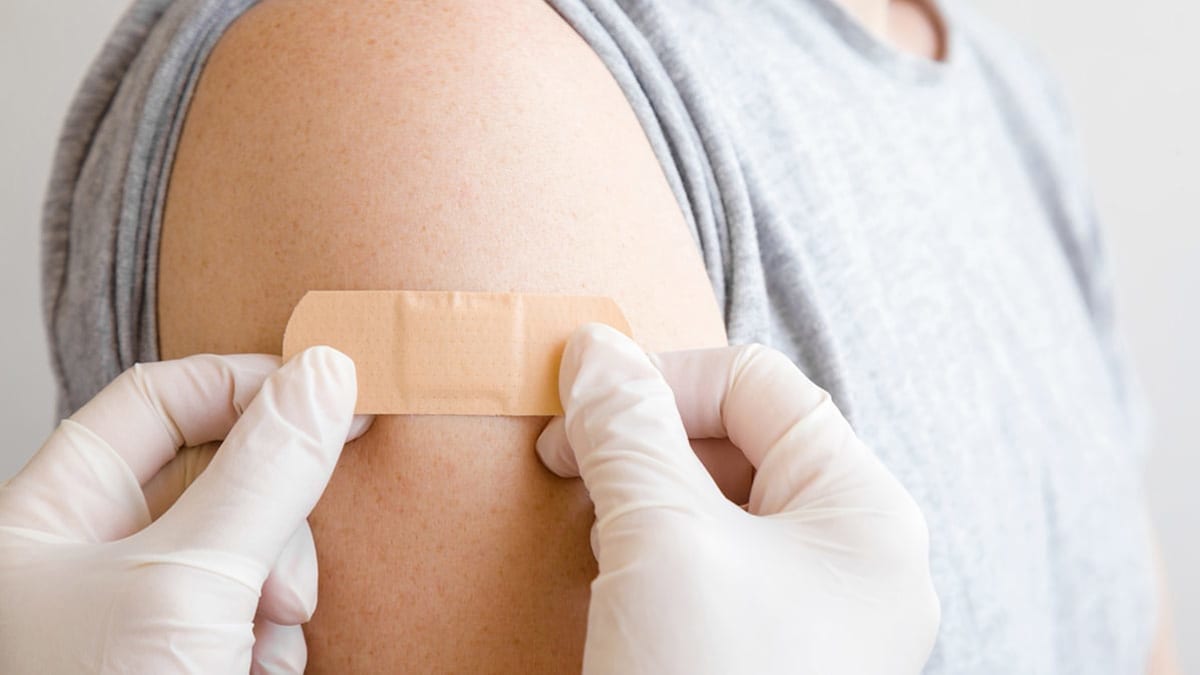 A healthcare worker placing a Band-Aid on patient's arm after a vaccine has been administered.