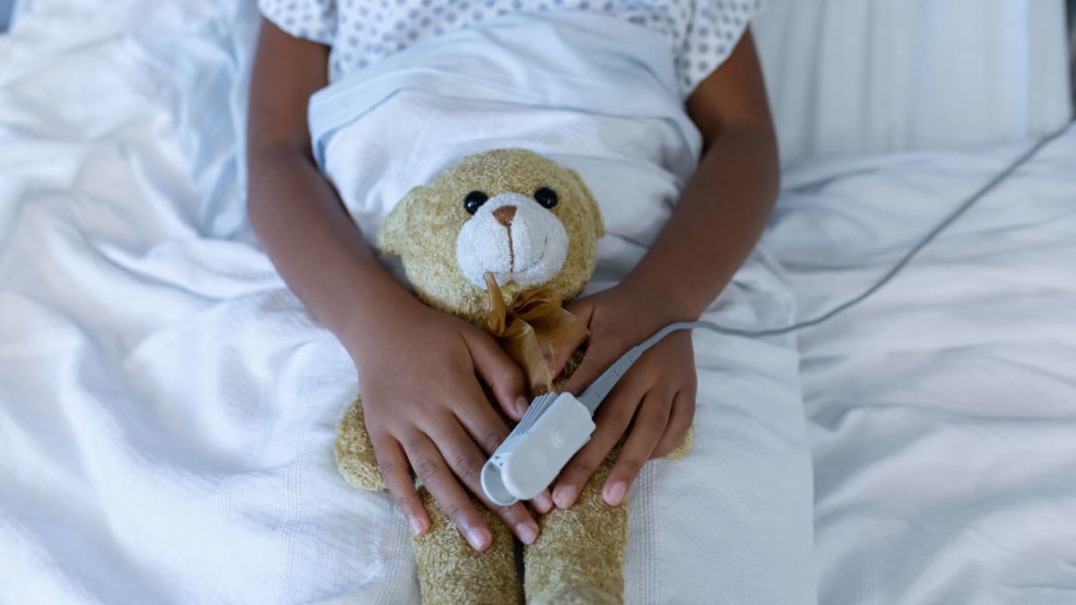 A child of color in a hospital bed with a teddy bear