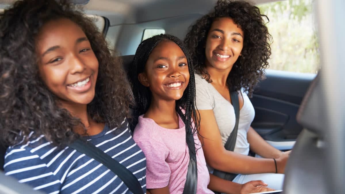 three kids of various ages wearing seatbelts in backseat of car