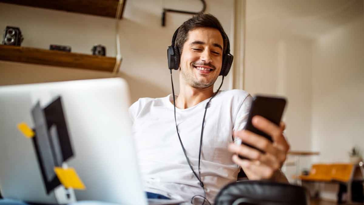 person wearing wired headphones while in front of computer and looking at phone
