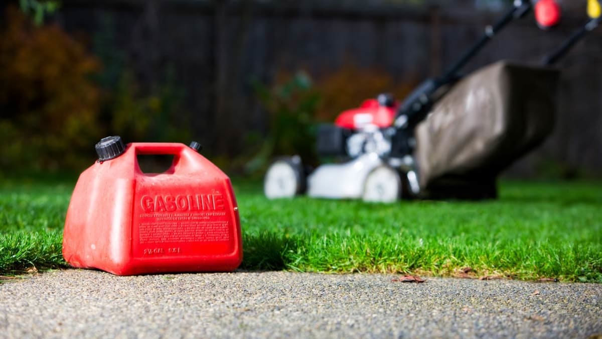 gasoline can on pavement with lawn mower in background