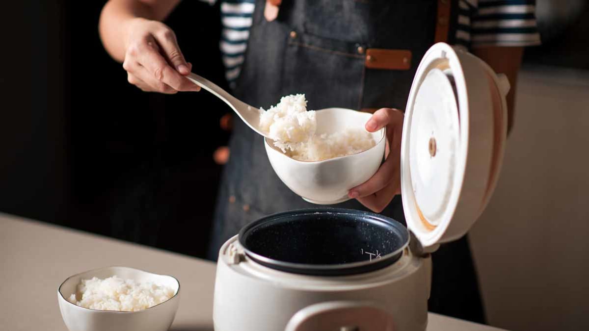 person scooping rice into bowl from rice maker