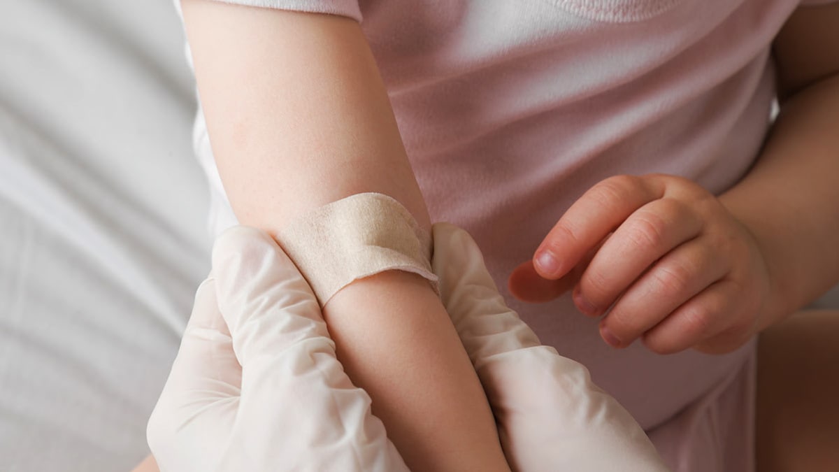 Doctor putting a band aid on a toddler after a blood draw.