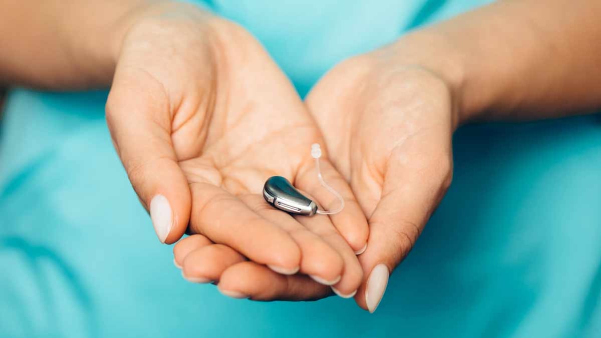 detail of person in teal scrubs holding hearing aid in palm of hands