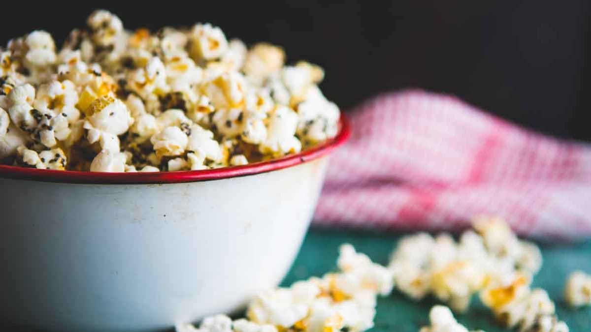 popcorn in white bowl with red border and popcorn spilled on side