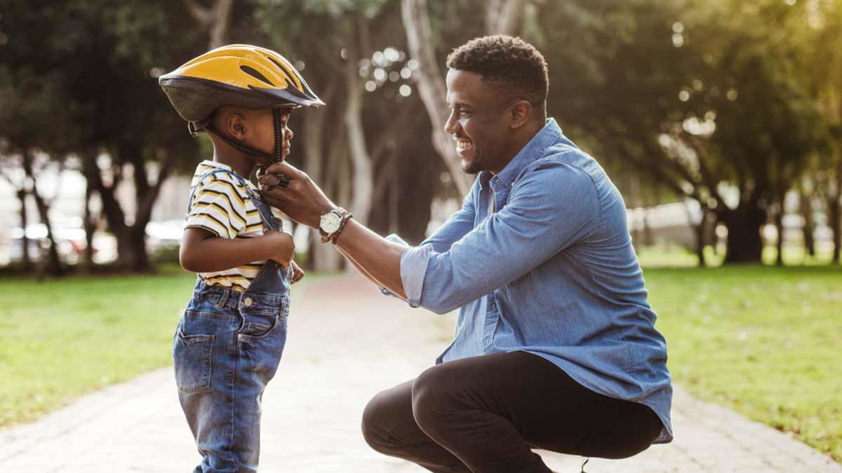 parent putting bike helmet on child in park