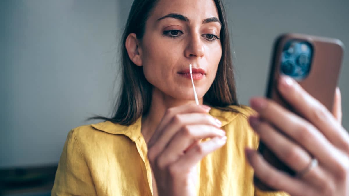 Woman holding smart phone and self-testing swab for Coronavirus/COVID-19
