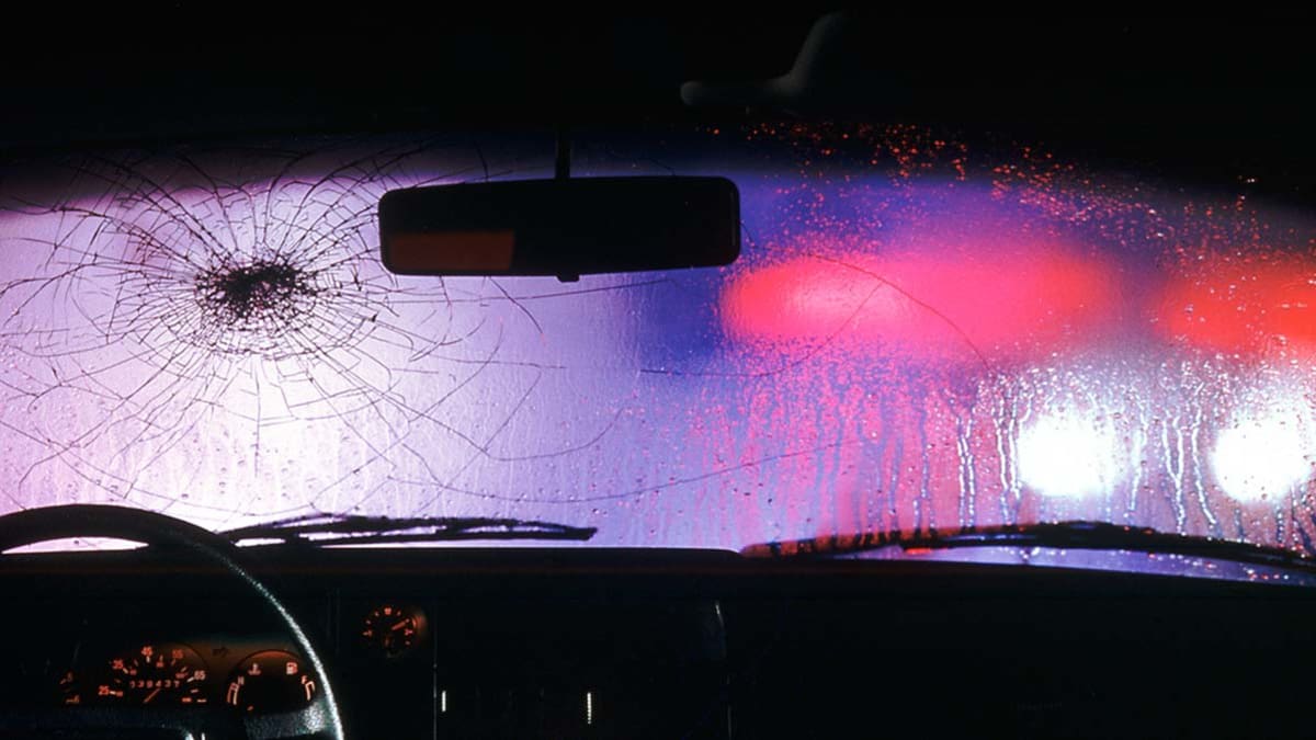A view from the inside of a car showing a cracked windshield and police lights