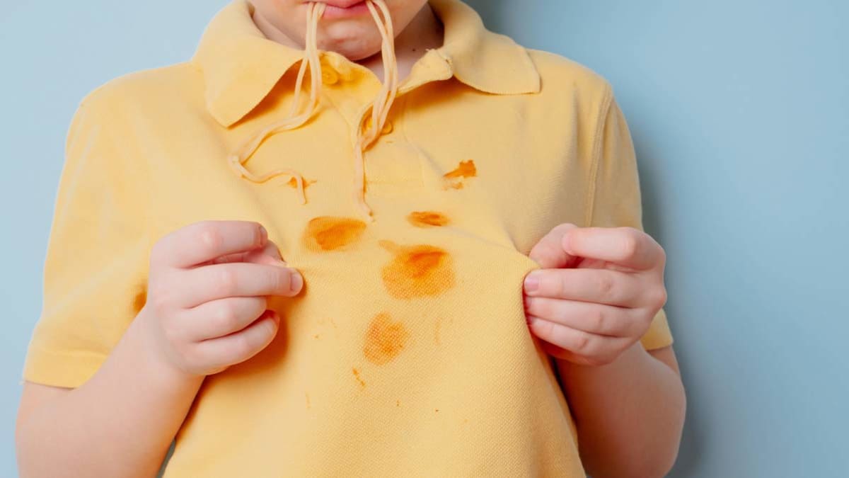 kid looking at tomato sauce stains on shirt with spaghetti hanging from house