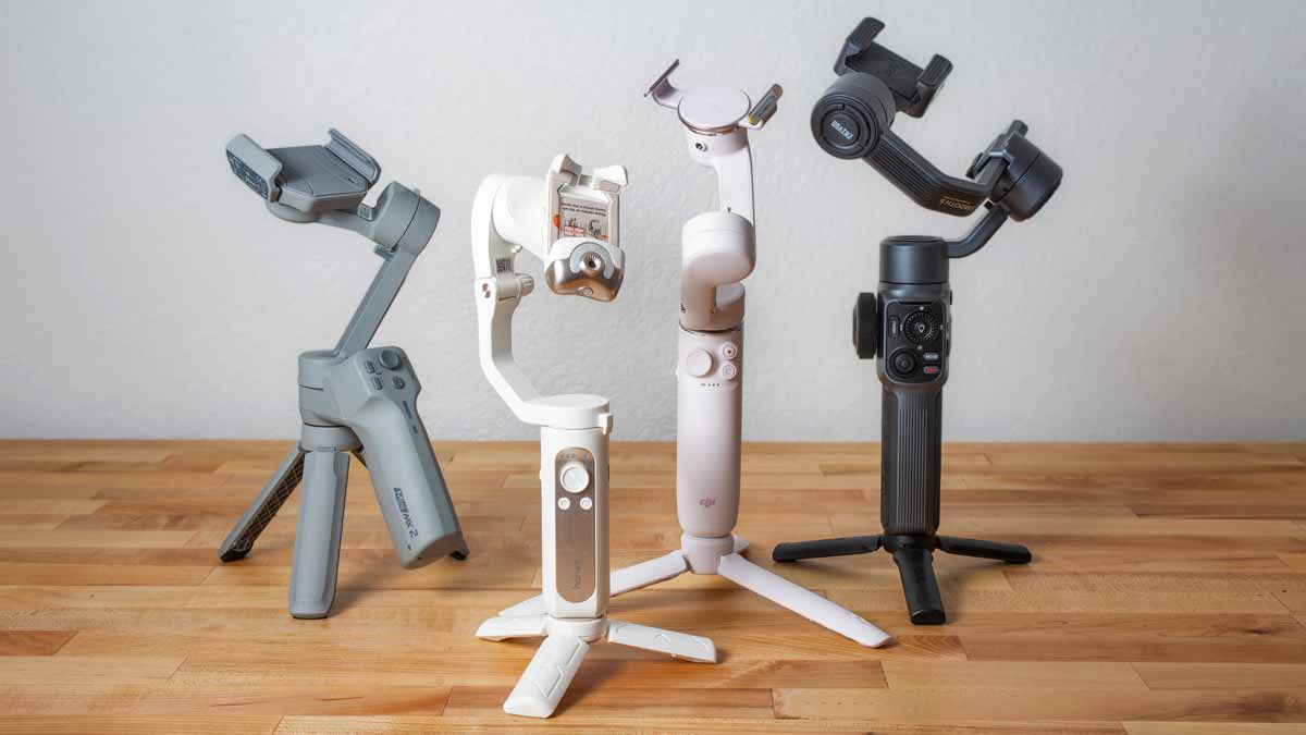 group of 4 smartphone gimbals on table: DJI OM 5, Zhiyun Smooth 5, MOZA Mini MX 2, Hohem iSteady V2