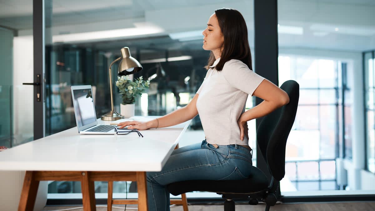 Woman experiencing back pain while working at desk