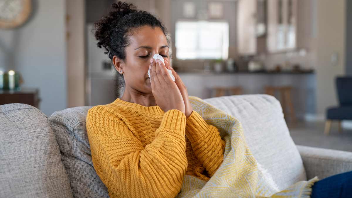 person sitting on couch blowing nose with blanket over them