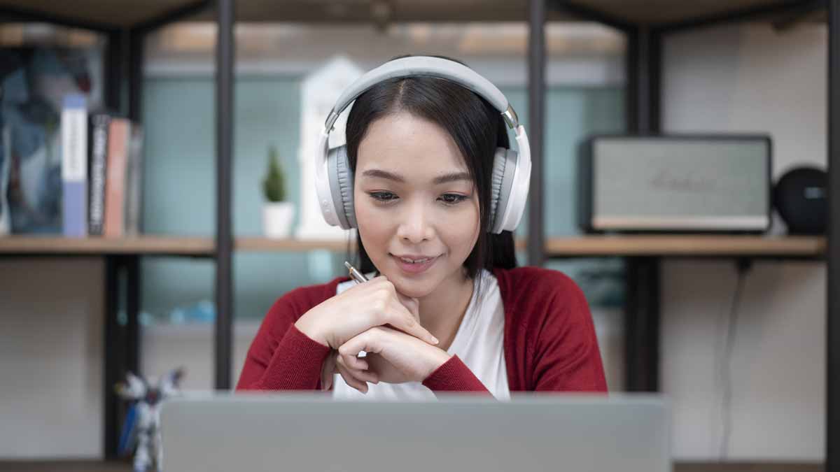 person wearing headphones sitting in front of laptop at table in home
