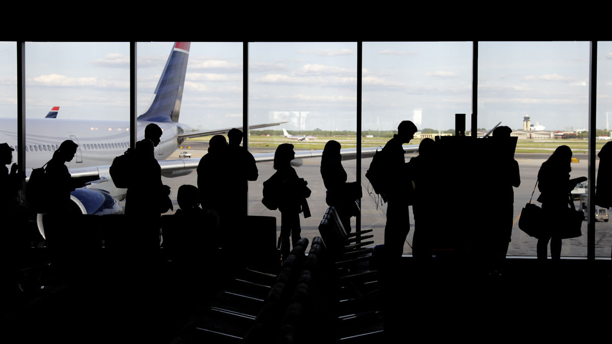 line of people in front of window at airport gate with airplanes outside behind them
