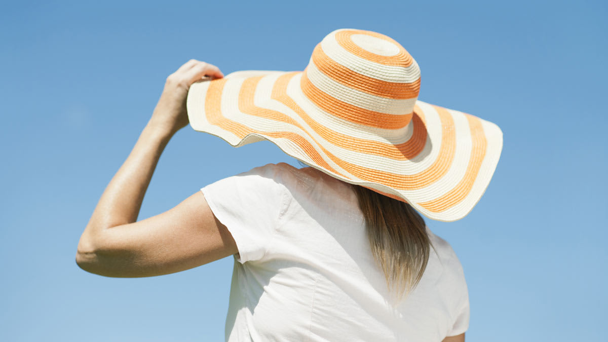 A woman in a wide brimmed hat from behind on a bright sunny day