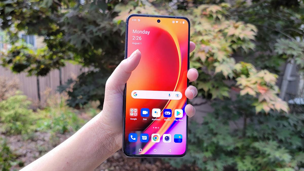 hand holding the OnePlus 10T phone with garden and tree in background