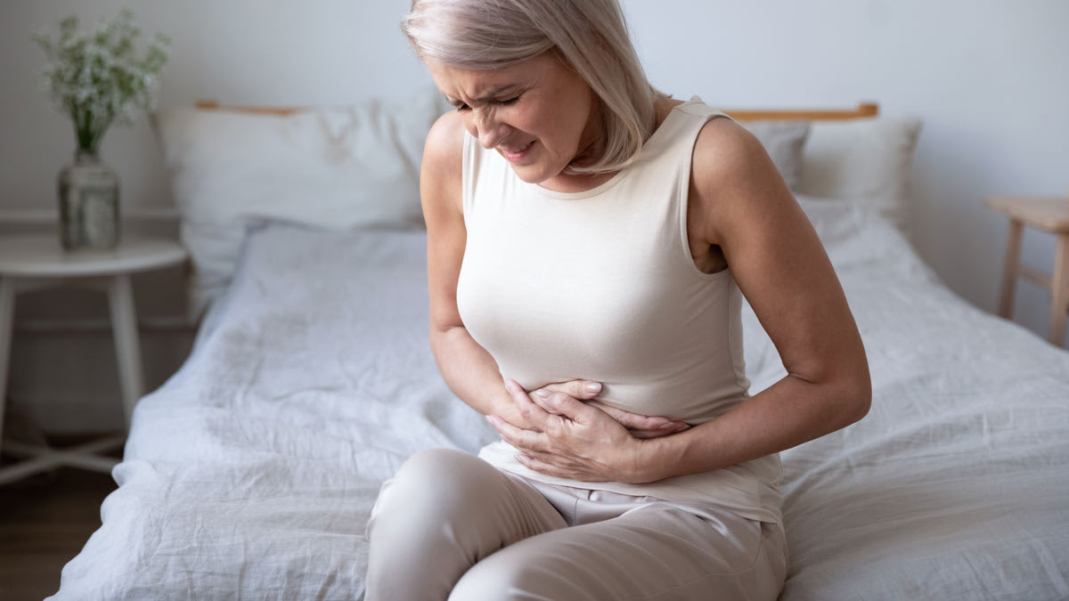 person sitting at edge of bed holding their abdominal area in pain