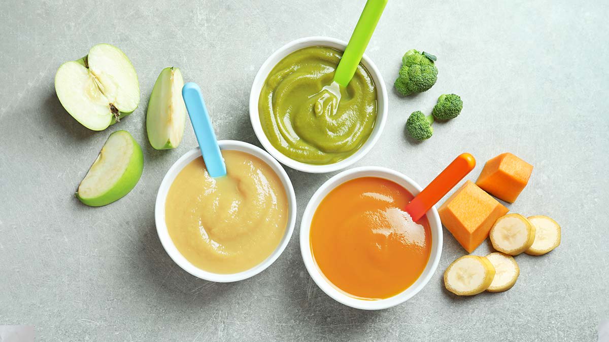Three bowls of homemade baby food with fresh produce sitting around them.