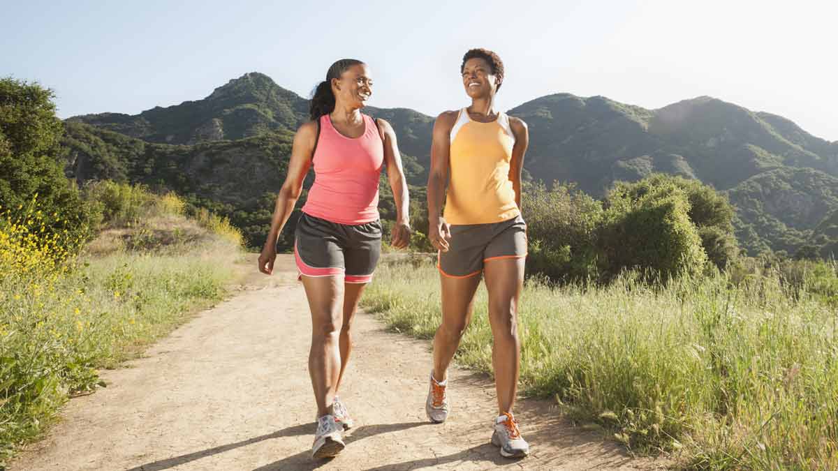 two people walking on dirt trail with mountains in background