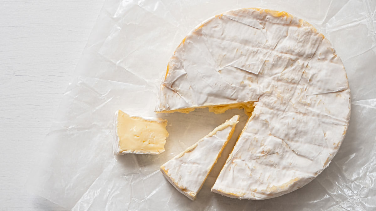 overhead view of wheel of brie on wax paper with 2 wedges cut out