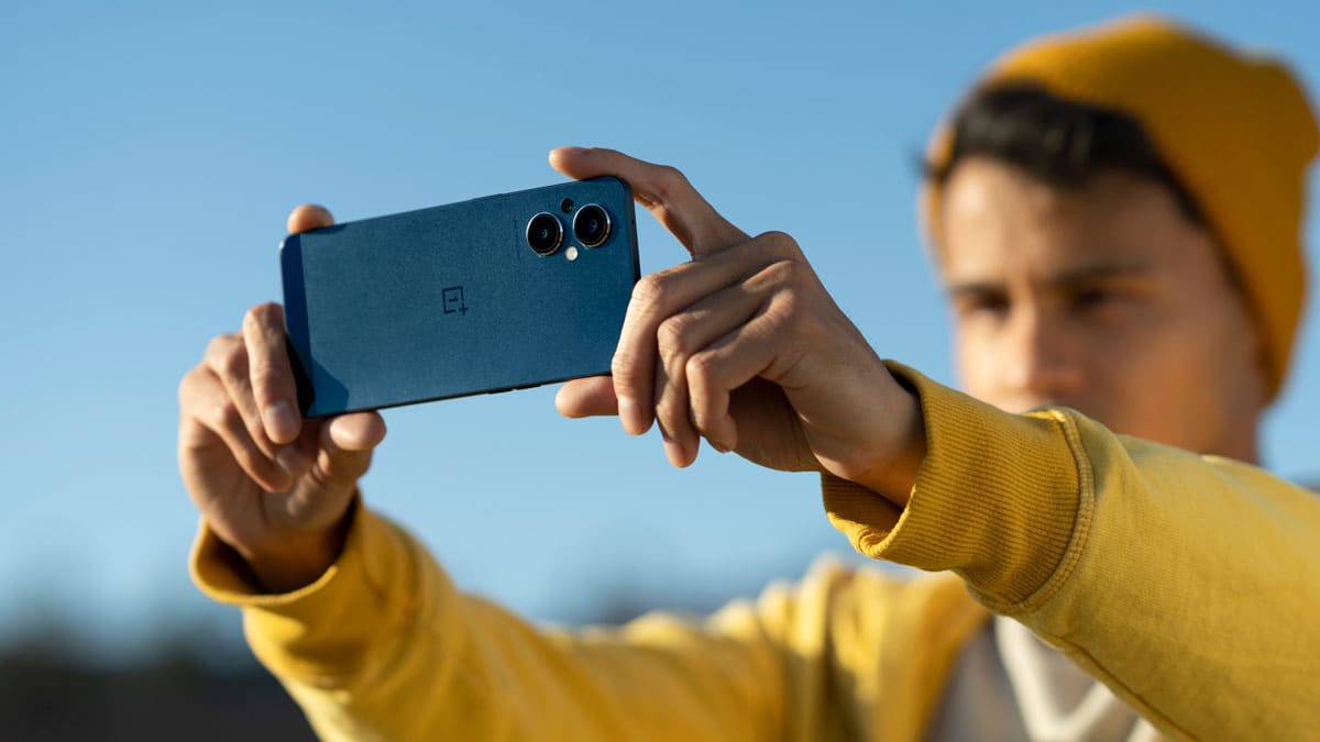 person in yellow shirt and hat holding OnePlus Nord N20 5G out in front of them