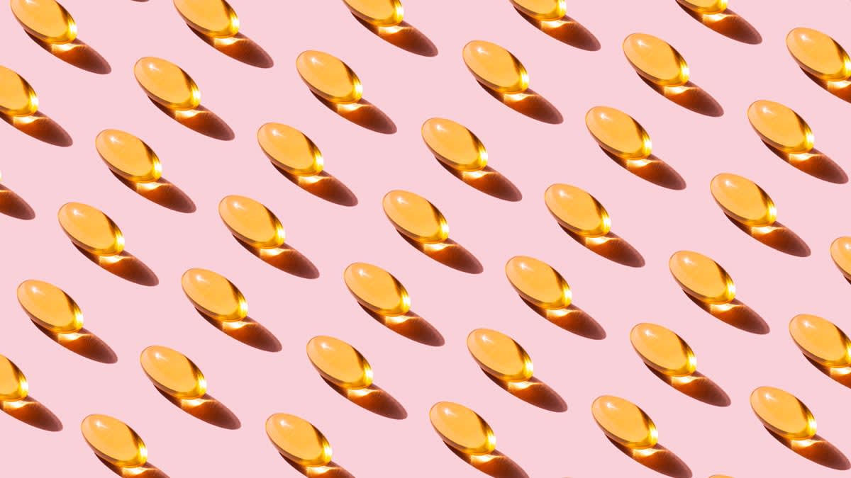 rows of vitamin D capsules on pink background