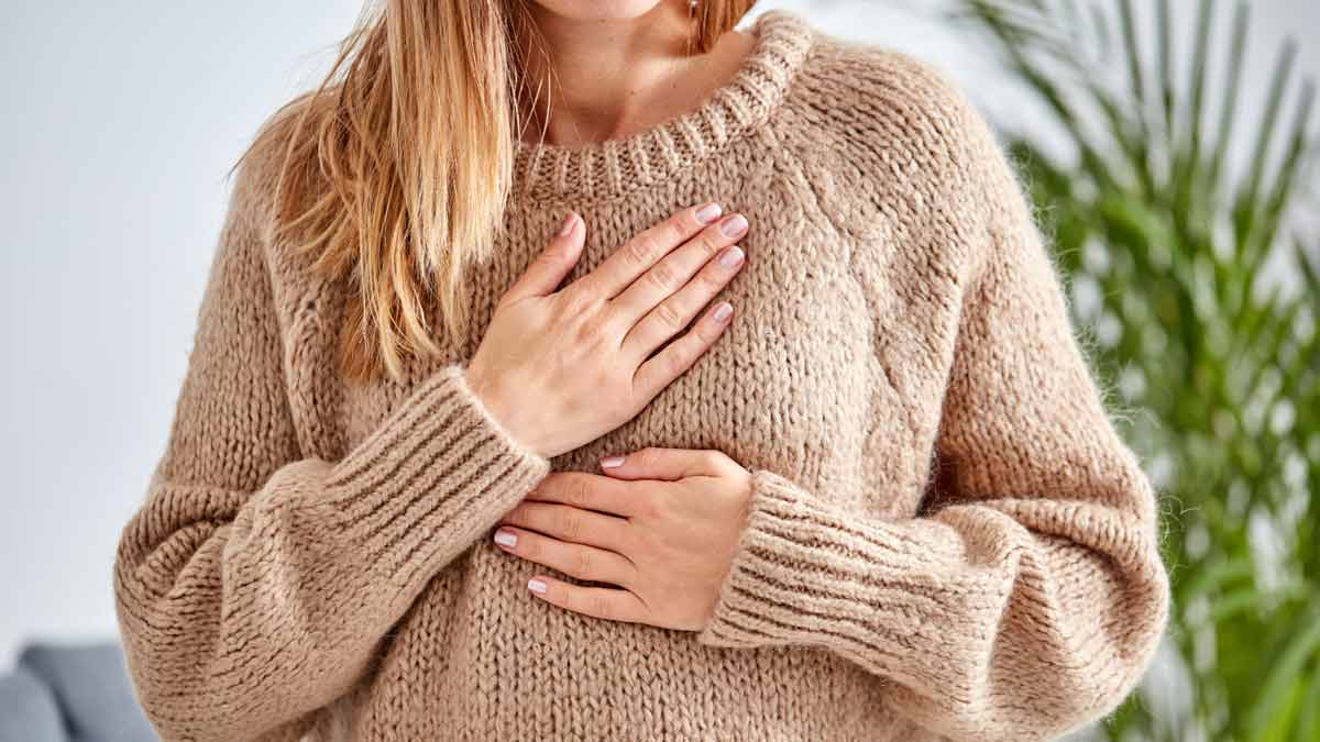 detail of person wearing beige sweater holding hands to chest as though they're in pain