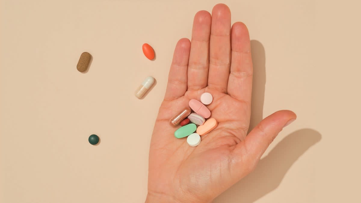 hand holding mixed supplements with 4 supplements on the surface next to the hand
