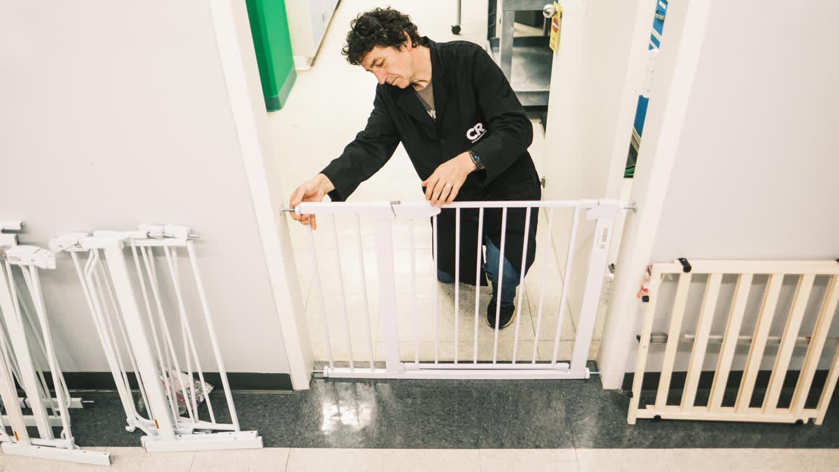 person in Consumer Reports lab coat installing baby gate on doorway in lab with other baby gates leaning against the wall
