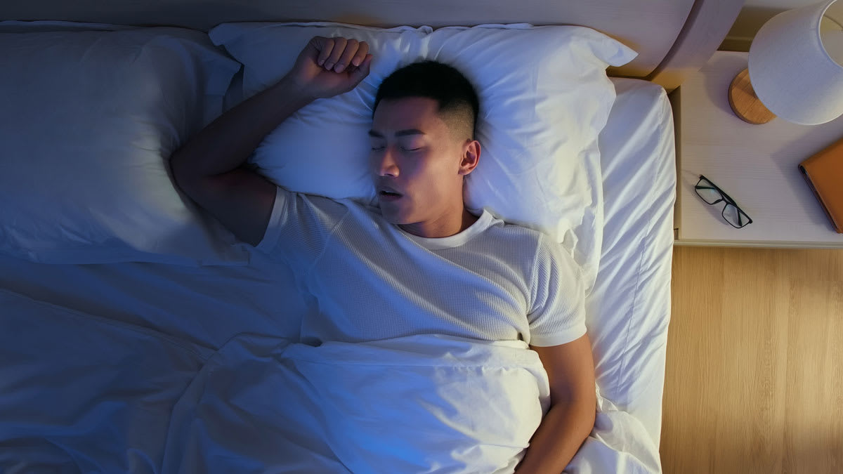 overhead view of person sleeping in bed with arm above head and their mouth open as though they're snoring