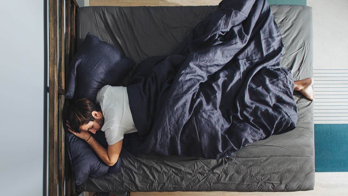 overhead view of person in bed sleeping on their stomach with grey sheets and blue comforter