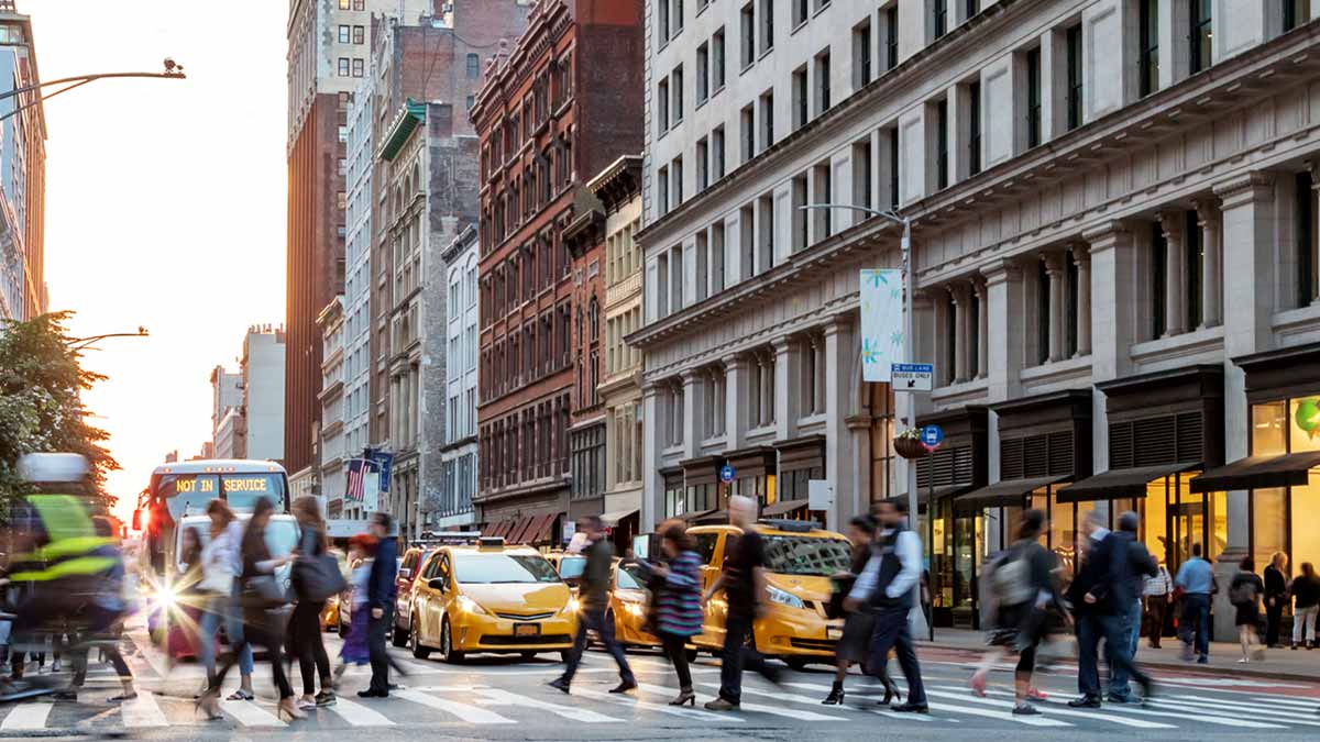 Multiple people walking across the street with cars stopped at a light in NYC