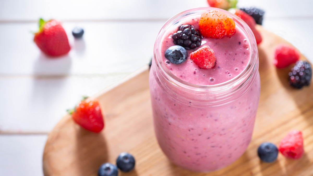 A finished smoothie—made with strawberries, blueberries, raspberries, and blackberries—sits atop a cutting board.