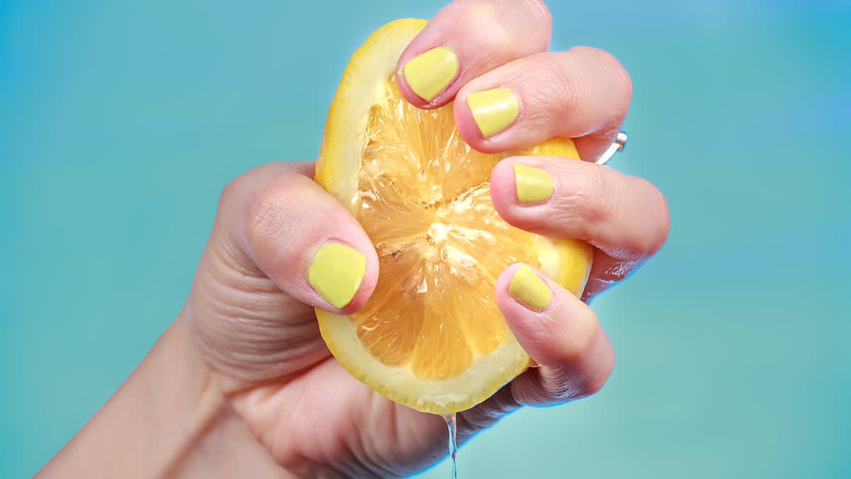 hand with yellow nail polish squeezing a lemon