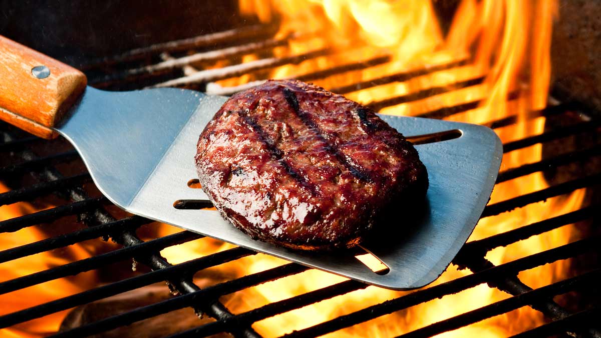 Burger on spatula over a flaming charcoal barbecue grill