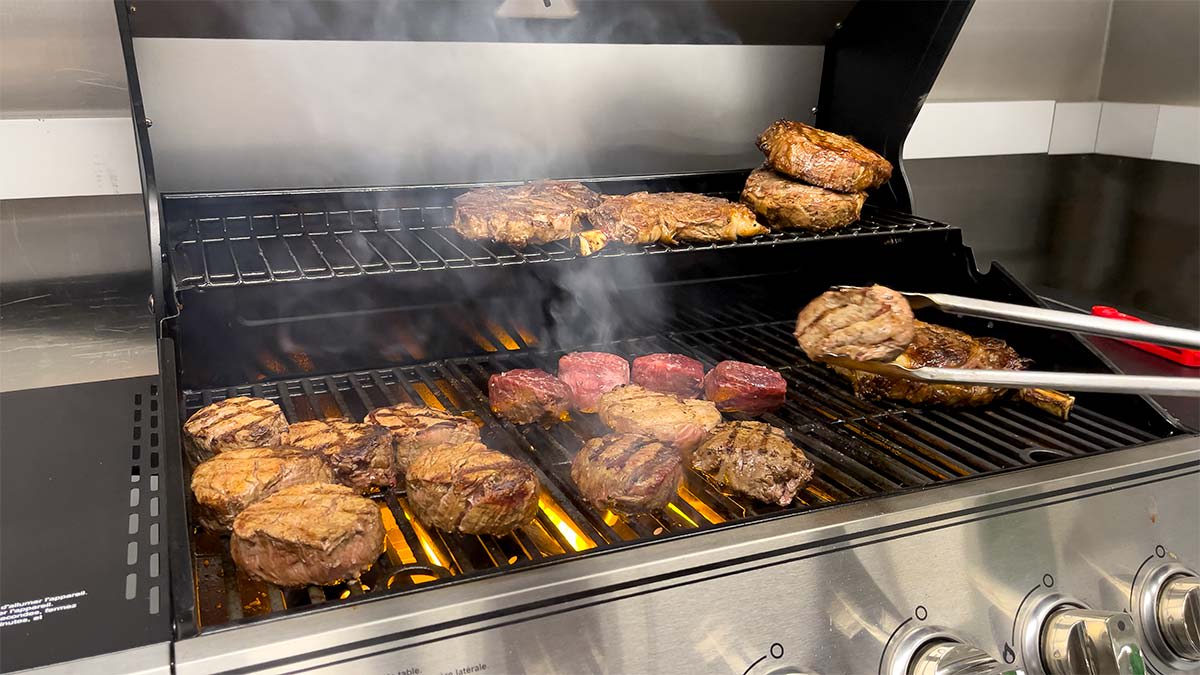 Filet mignons and ribeyes cooking on a grill
