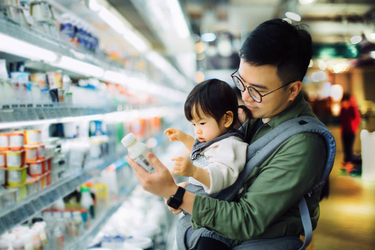 parent holding baby in front baby carrier while looking at label in grocery store aisle