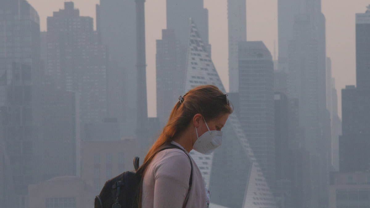 A woman wears a face mask as smoke continues to shroud the sun as it rises behind the skyline of Manhattan in New York City on June 7, 2023, as seen from Weehawken, New Jersey.