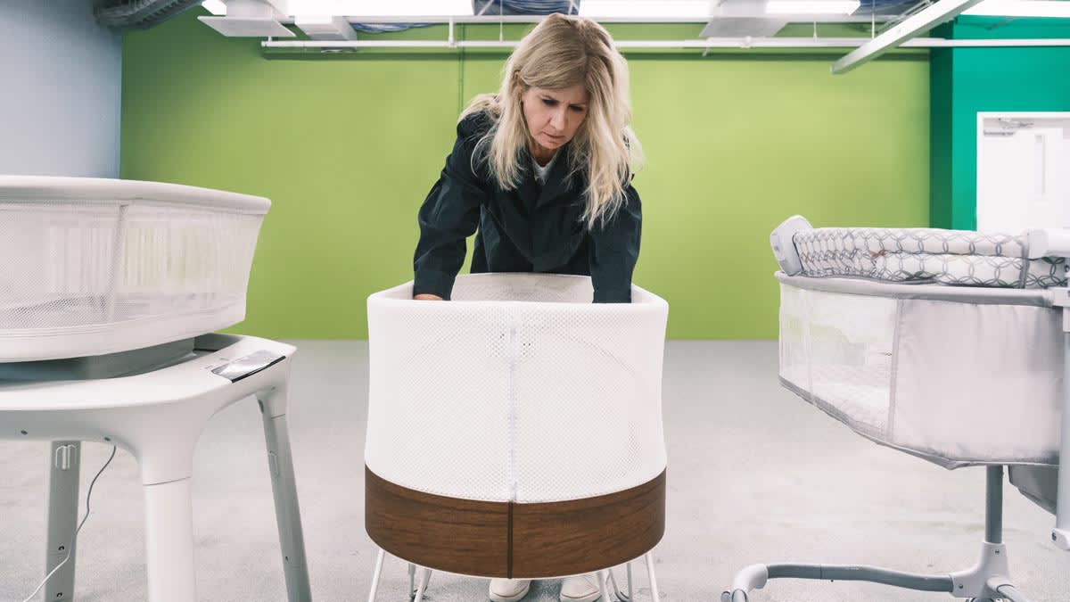 person leaning into Snoo bassinet with other bassinets around them