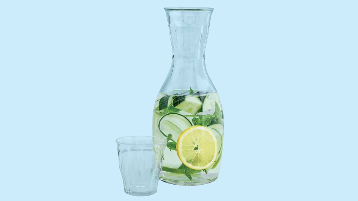 empty glass and pitcher of water with slices of lemon, cucumber, and basil leaves