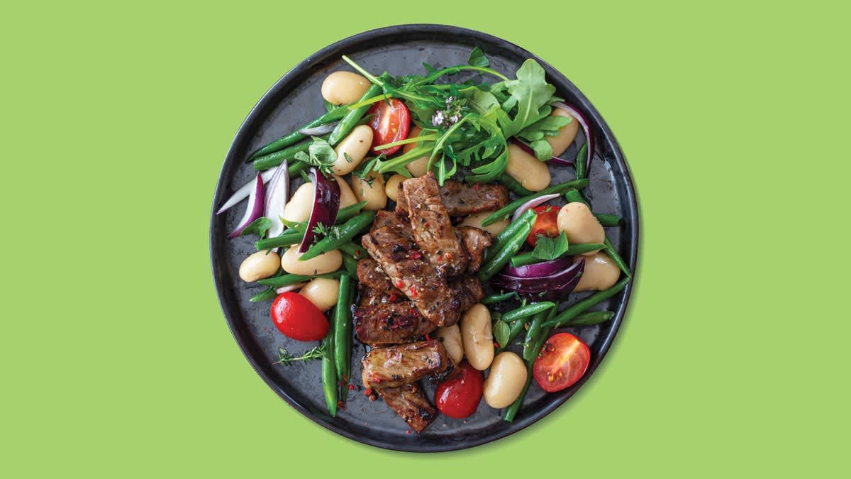overhead view of plate with beef strips, beans, green beans, grape tomatoes, red onion, and arugula