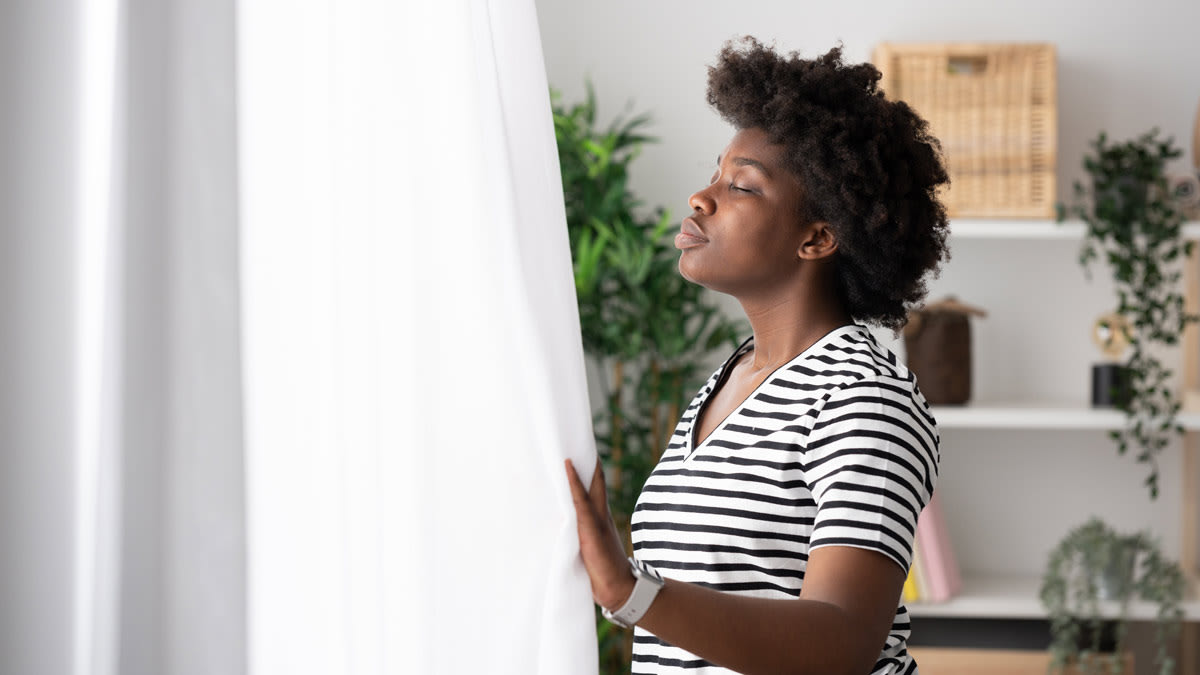 person standing in front of window holding curtain while breathing deeply