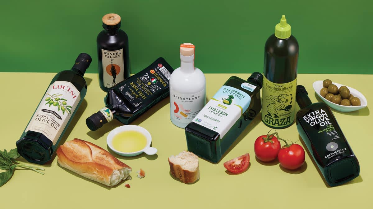 Olive oils on a table with bread, tomatoes, and olives.