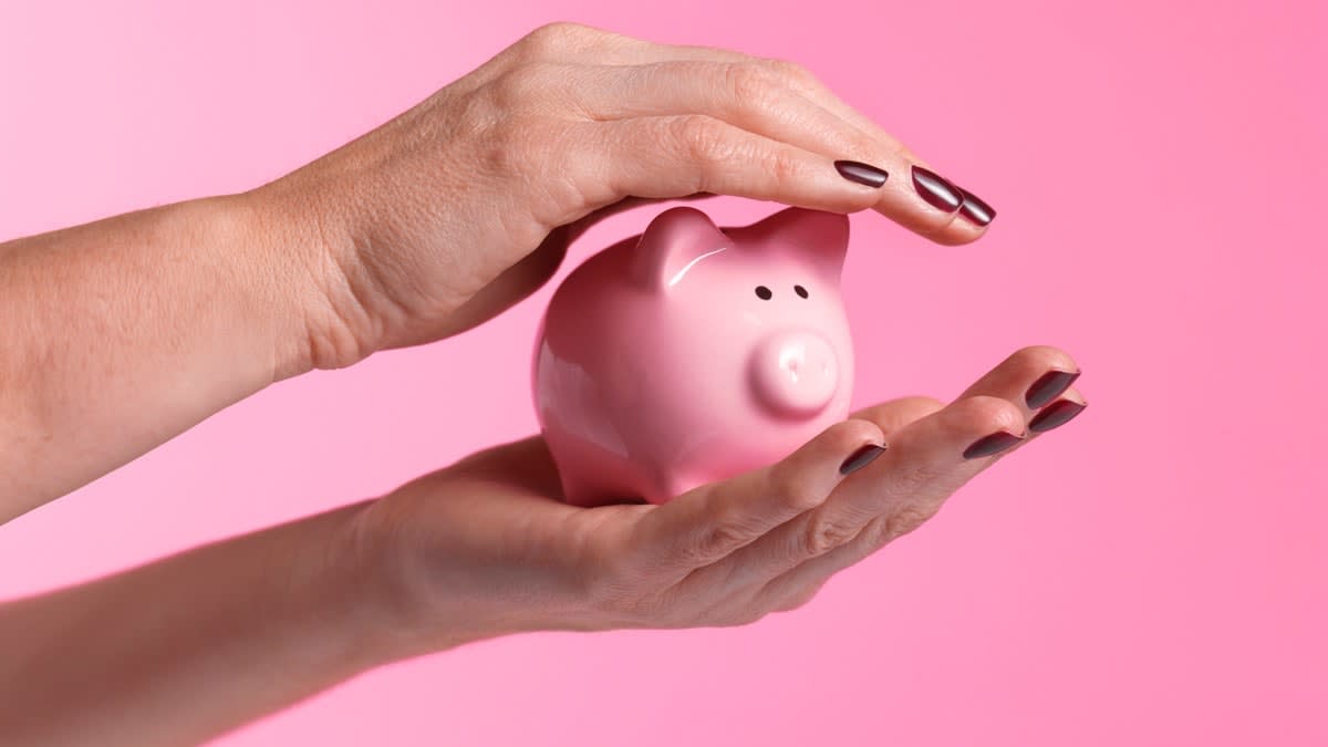 one hand holding and the other hand protecting a pink piggy bank