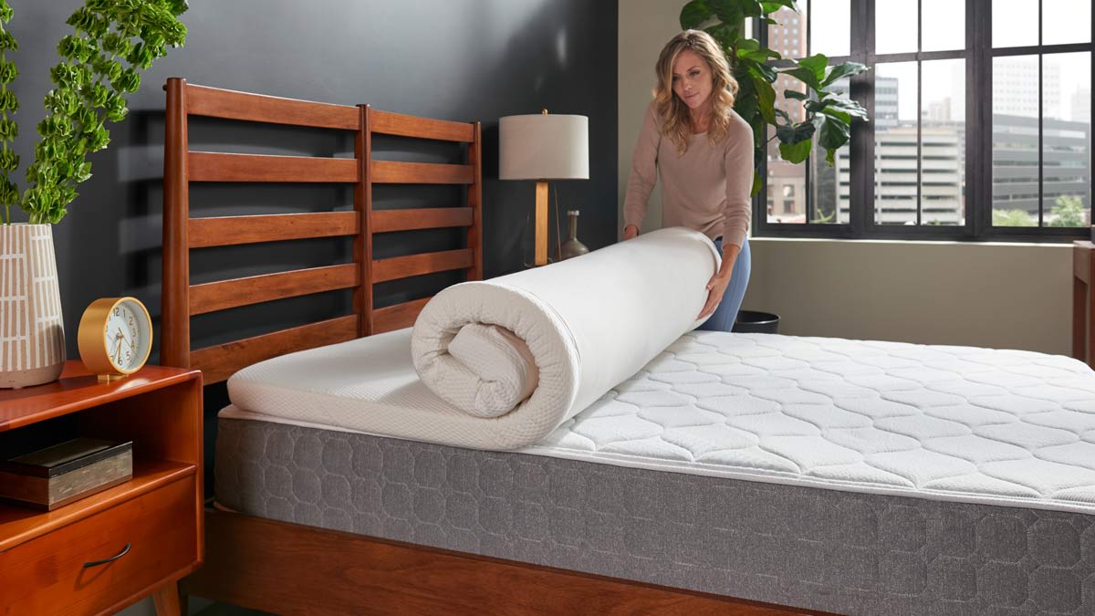 person unrolling Tempur-Pedic Supreme Topper mattress topper on mattress with wooden bedframe