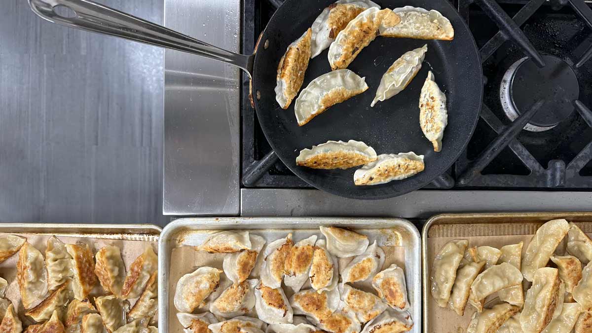 a frying pan with frozen dumplings being cooked, next to pans of cooked dumplings at a Consumer Reports food lab