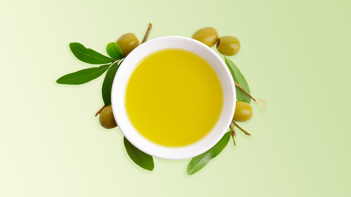 A bowl of olive oil with some olives and olive branches next to it